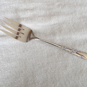May include: A silver fork with an ornate handle. The fork has three tines and a rounded handle with a floral design.
