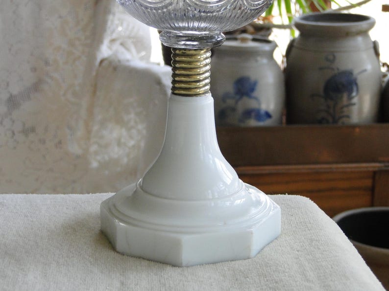 May include: A white, octagonal-based lamp with a clear, textured glass top. The lamp features a gold-colored, threaded metal section connecting the base to the glass. The lamp is likely a decorative or functional lighting fixture.