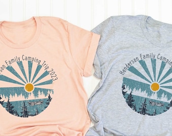 May include: Two t-shirts with a vintage sunburst design and the text "Henderson Family Camping Trip 2023". One shirt is peach and the other is gray.