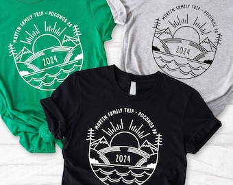 May include: Three t-shirts with a graphic design of a mountain range with a sun and the text "Martin Family Trip - Poconos PA 2024". The shirts are green, grey, and black.