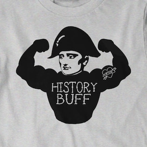 May include: A grey t-shirt featuring a black illustration of Napoleon Bonaparte flexing his muscles. The illustration includes the text "HISTORY BUFF" and a small heart with the word "LOVE" inside. The text "BUY ANY 3, 4TH FREE! CODE BOOOTE" is printed in yellow at the bottom of the shirt.