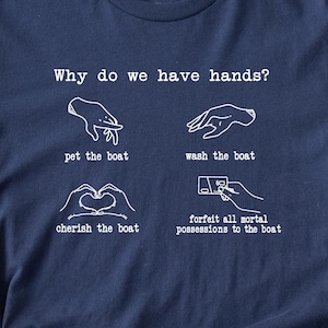 Puede incluir: Camiseta azul marino con texto e ilustraciones en blanco. El texto dice "¿Por qué tenemos manos?" con cuatro ilustraciones y leyendas: "acariciar el barco", "lavar el barco", "apreciar el barco" y "renunciar a todas las posesiones mortales al barco". La marca "Boootees" está en la parte inferior.