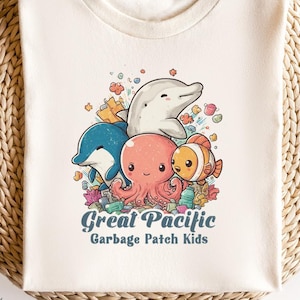 May include: Off-white t-shirt with a marine-themed graphic featuring a dolphin, octopus, and clownfish. The text "Great Pacific Garbage Patch Kids" is printed below the illustration. The shirt is displayed on a woven surface.