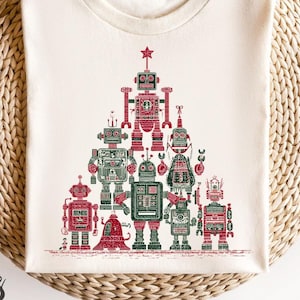 May include: Cream-colored t-shirt featuring a Christmas tree design made of red and green robots. The robots have various shapes and sizes, with a star at the top. The text "bootees" is printed on the bottom left.
