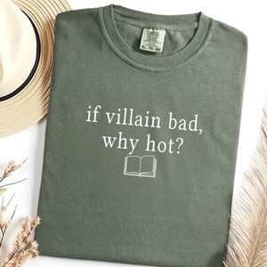May include: An olive green t-shirt with the text "if villain bad, why hot?" in white, along with a small open book graphic. The shirt is a crew neck style.