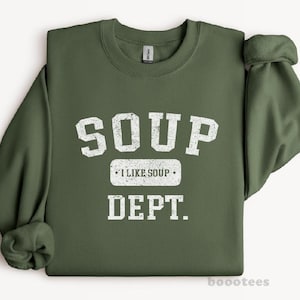 May include: Olive green sweatshirt with the words "SOUP I LIKE SOUP DEPT." in white, block letters. The sweatshirt has a crew neck and long sleeves. The text is centered on the front of the shirt.
