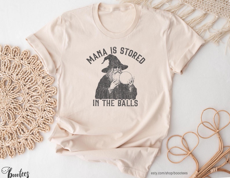 A funny fantasy shirt depicting a wizard holding a crystal ball that says mana is stored in the balls.