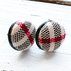 May include: A pair of black and white plaid fabric earrings with red accents. The earrings are round and have a black backing.