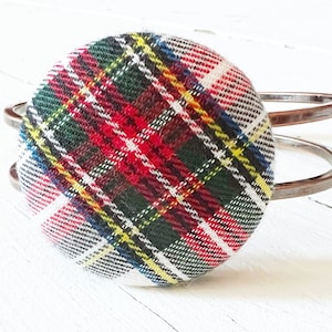 May include: A silver metal bangle bracelet with a red, white, green, and yellow plaid fabric button.
