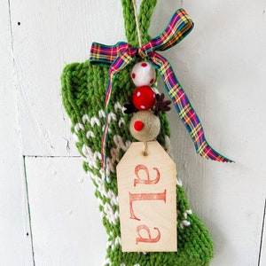 May include: Green and white knitted Christmas stocking with a red and green plaid ribbon and a tag that says "Ella".