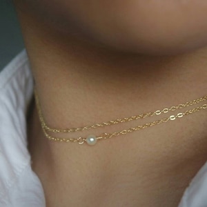 May include: A delicate gold chain necklace with a single pearl pendant. The necklace is layered, with two chains of different thicknesses.