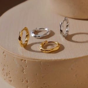 Könnte beinhalten: Eine Sammlung von vier kleinen Creolen mit einer gedrehten, unregelmäßigen Oberflächenstruktur. Zwei der Creolen haben ein poliertes Gold-Finish, während die anderen beiden ein poliertes Silber-Finish aufweisen, alle mit Klappverschluss.