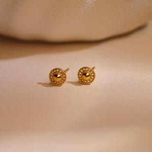 Könnte beinhalten: Eine weiße Keramik-Tasse mit schwarzem Henkel und dem Text "But First, Coffee" in fetter, schwarzer Schrift. Die Tasse steht vor einem verschwommenen Hintergrund, der eine gemütliche Umgebung suggeriert.