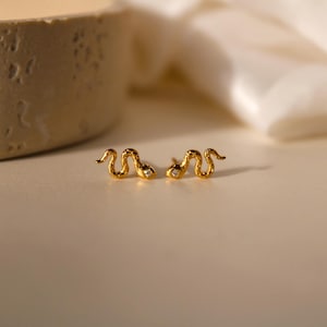 May include: A pair of gold snake earrings with a small clear stone in each eye.