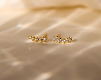 May include: A pair of gold earrings with a curved row of small, clear cubic zirconia stones.