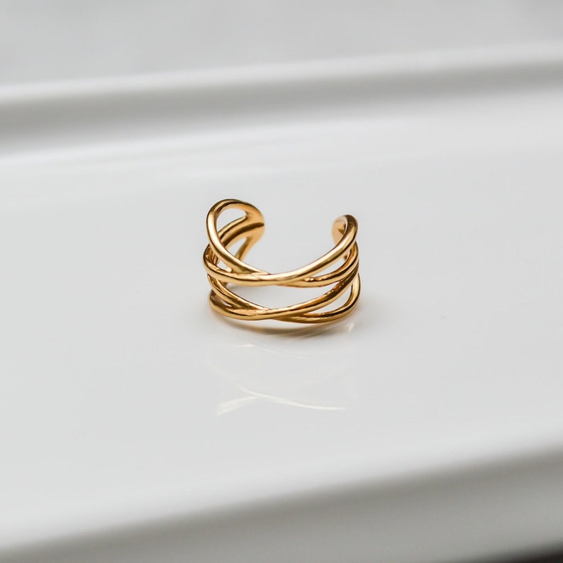 Puede incluir: Un pendiente de oreja dorado con un dise&ntilde;o simple e entrelazado. El pendiente est&aacute; hecho de una sola pieza de metal que se dobla en forma de curva.