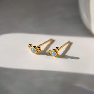 Könnte beinhalten: Ein Paar goldene Ohrringe mit einem kleinen Opal und zwei winzigen Diamanten an jedem Ohrring.