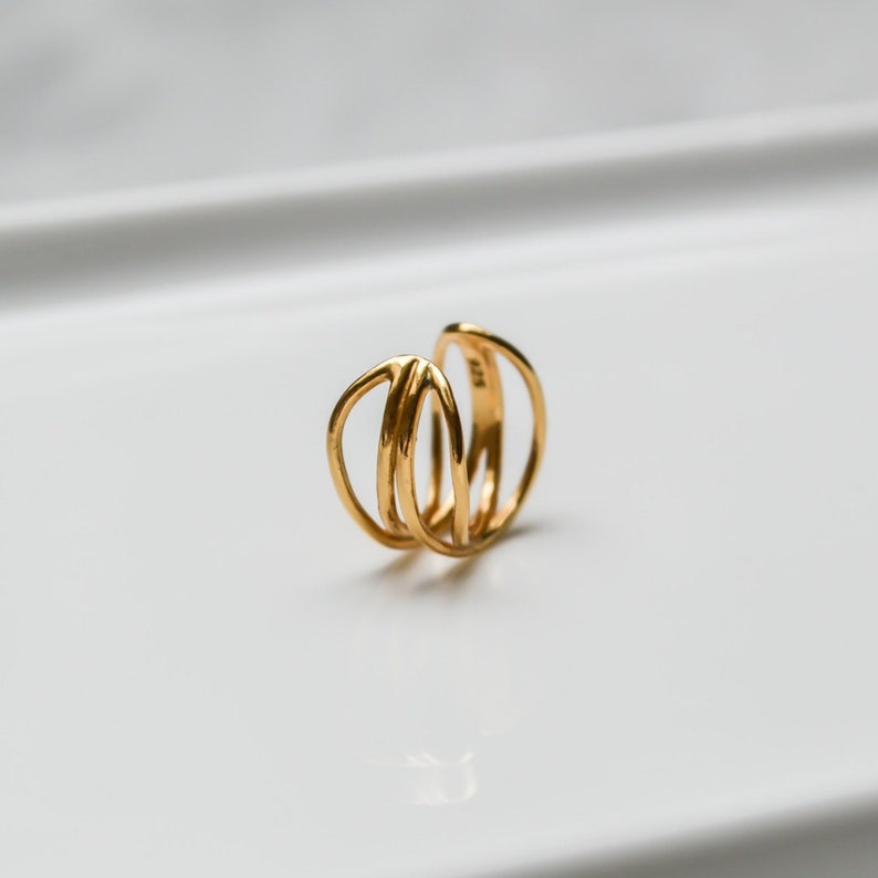 Puede incluir: Pendiente de oreja dorado con un dise&ntilde;o simple y moderno. El pendiente est&aacute; hecho de tres anillos superpuestos.