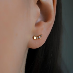 Könnte beinhalten: Goldene Stern- und Kristall-Ohrstecker. Die Ohrringe haben die Form eines Sterns mit drei kleinen Kristallen.