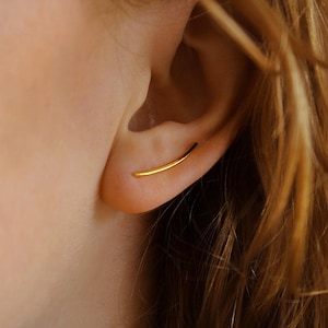 May include: A gold ear cuff earring with a curved bar design. The earring is worn in the upper part of the ear.