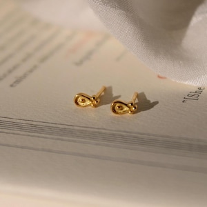 Könnte beinhalten: Ein Paar goldfarbene Ohrstecker mit einem kleinen, tropfenförmigen Design. Jeder Ohrstecker hat einen kleinen, runden Akzent an der Seite.