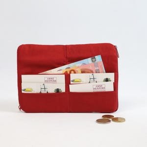May include: A red fabric wallet with multiple pockets and a zip closure. The wallet contains cash and cards with the text "Anne Hermine" printed on them.