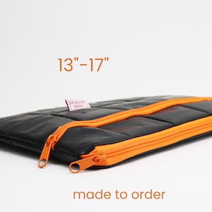 Könnte beinhalten: Schwarze, gesteppte Laptoptasche mit orangefarbenem Reißverschluss. Die Tasche ist auf Bestellung gefertigt und passt für Laptops zwischen 13" und 17".