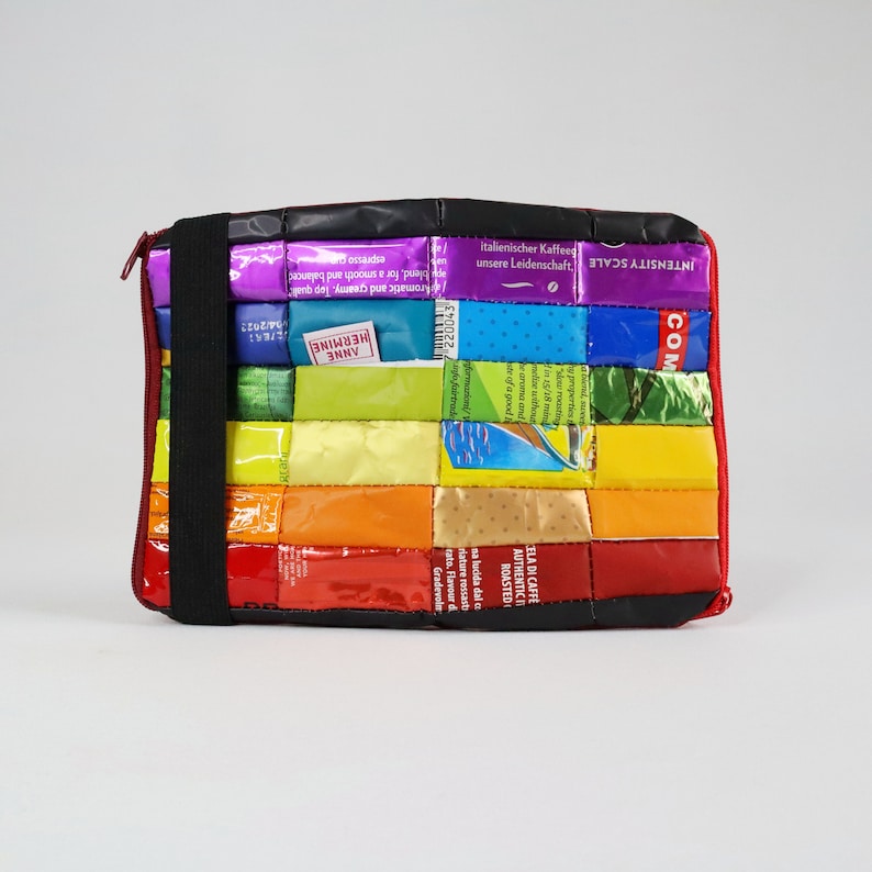 May include: A colourful laptop sleeve made from recycled coffee packaging. The sleeve is a patchwork of different coloured squares with text in German and Italian. The text includes "italienischer Kaffee" and "unsere Leidenschaft".