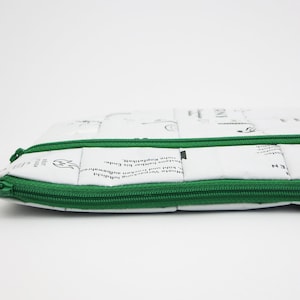 以下が含まれることがあります： 緑色のジッパーが付いた白いジッパーポーチ。ポーチはリサイクル素材で作られており、さまざまなテキストが印刷されています。