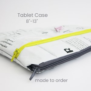 Puede incluir: Una funda para tablet blanca con una cremallera amarilla y un tirador de cremallera gris. La funda está hecha de materiales reciclados y tiene un diseño de patchwork. El texto "Tablet Case 8"-13" made to order" está impreso en la funda.