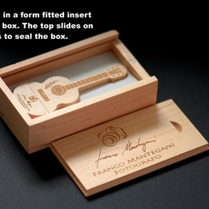 K&ouml;nnte beinhalten: Eine Holzkiste mit einem Schiebedeckel, die einen h&ouml;lzernen USB-Stick in Form einer Gitarre enth&auml;lt. Die Kiste ist mit dem Text "froms Martyni FRANCO MANTEGANI FOTOGRAFO" graviert.