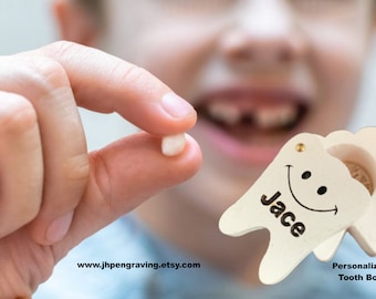 Può includere: Una scatola per denti in legno bianco con un viso sorridente e il nome "Jace" inciso su di essa. Un bambino tiene un dente da latte in mano, pronto a metterlo nella scatola. Scatola per denti personalizzata.