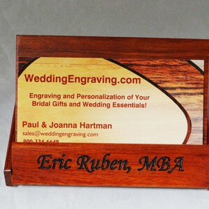 May include: A wooden business card holder with a business card inside. The business card is for WeddingEngraving.com and has the text "Engraving and Personalization of Your Bridal Gifts and Wedding Essentials!"  The business card holder has the name "Eric Ruben, MBA" engraved on the front.