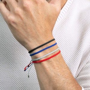 May include: Four bracelets stacked on a person's wrist. The bracelets are black, blue, gray, and red.