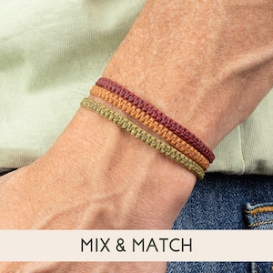 May include: Three braided bracelets in shades of red, orange, and green. The bracelets are worn on a person's wrist. The text "MIX & MATCH" is visible below the bracelets.