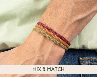 May include: Three braided bracelets in shades of red, orange, and green. The bracelets are worn on a person's wrist. The text "MIX & MATCH" is visible below the bracelets.