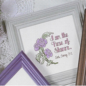 May include: A framed cross-stitch with a purple floral design and the text "I am the Rose of Sharon.  Sol. Song 2:1"
