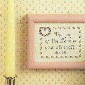 Puede incluir: Un bordado de punto de cruz enmarcado en rosa con fondo blanco y el texto "The joy of the Lord is your strength.  Neh. 8:10".