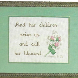 May include: A framed cross-stitch with a green mat and gold frame. The cross-stitch features a floral design and the text "And her children arise up and call her blessed. Proverbs 31:28"
