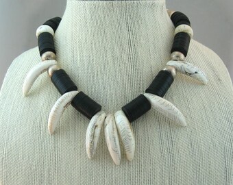 May include: A black and white necklace with large, white, tooth-shaped beads and black, round beads. The necklace is on a white mannequin.