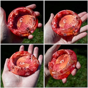 May include: A round, translucent resin ashtray featuring a vibrant gradient of red, orange, and yellow hues. The surface displays a textured, marbled effect with embedded glitter and small, iridescent flecks throughout the circular structure.
