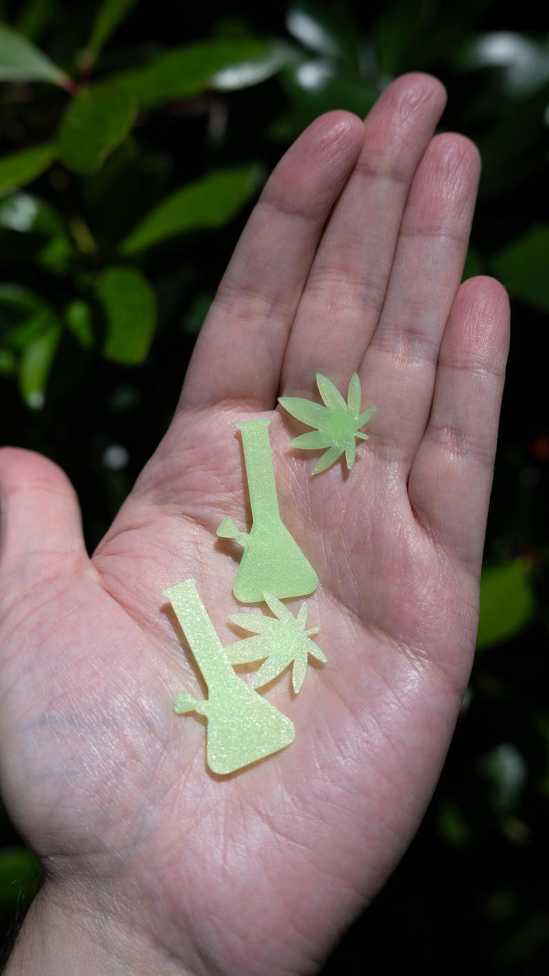 May include: Two small, flat, light green, glow-in-the-dark decorative shapes in the form of water pipes and two matching light green leaf-shaped cutouts, all featuring a subtle, fine-grained, shimmering texture on their surfaces.