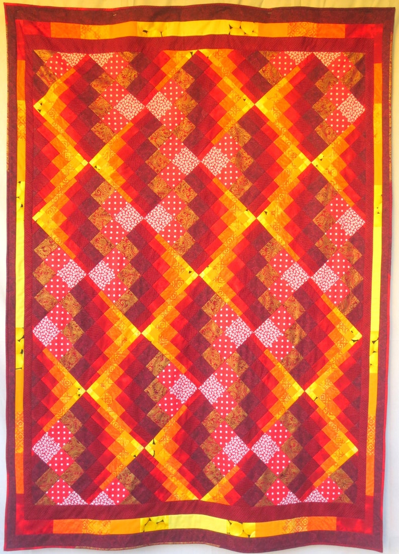 May include: A quilt with a diamond pattern in shades of red, orange, and yellow. The quilt is made of different fabrics with various patterns, including polka dots, paisley, and floral prints.