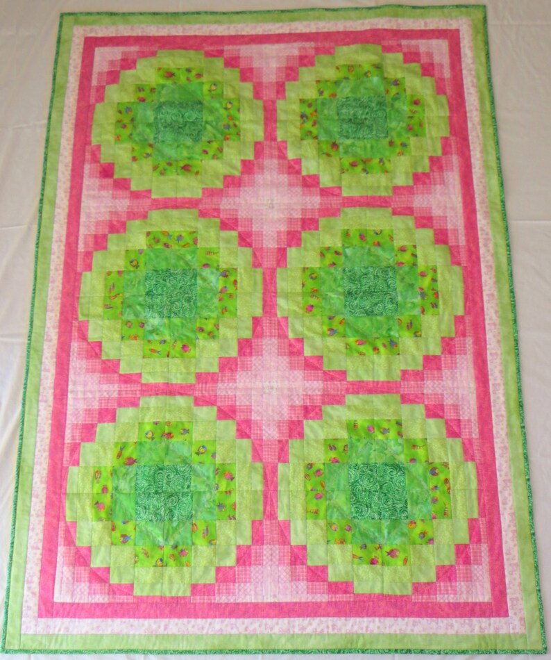 May include: A quilt with a pink and green patchwork design. The quilt is made up of squares of different sizes, with a central square in each section. The quilt is edged with a white border.