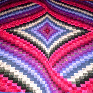 以下が含まれることがあります： 中央にダイヤモンド模様のカラフルなキルト。キルトはピンク、パープル、ブルー、ブラックの様々な色合いの生地で作られています。