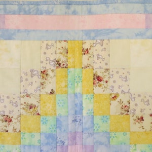 May include: A patchwork quilt with a geometric design featuring squares of yellow, blue, green, and pink fabric. The quilt is made with a variety of floral and patterned fabrics.