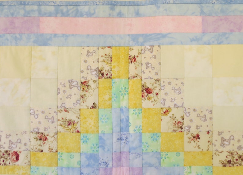 May include: A patchwork quilt with a geometric design featuring squares of yellow, blue, green, and pink fabric. The quilt is made with a variety of floral and patterned fabrics.