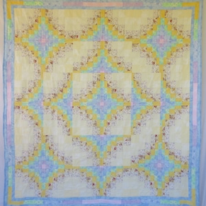 May include: A yellow, blue, and pink quilt with a geometric pattern. The quilt is made of squares and rectangles, and the colors are arranged in a repeating pattern.