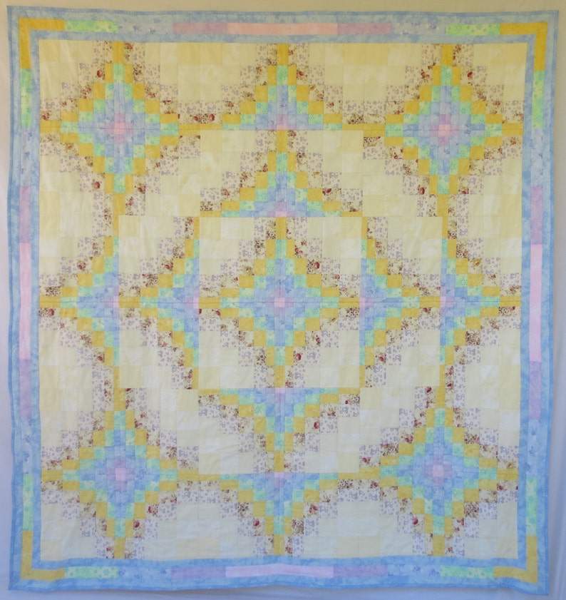 May include: A yellow, blue, and pink quilt with a geometric pattern. The quilt is made of squares and rectangles, and the colors are arranged in a repeating pattern.