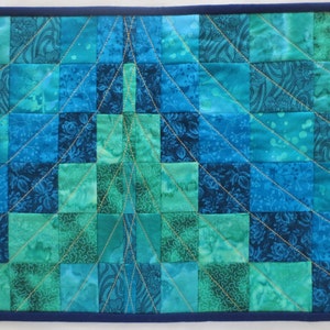 May include: A blue and green patchwork quilt with a geometric design. The quilt is quilted with gold thread and has a navy blue border.